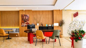 Área de recepção de hotel com balcão, assentos e uma planta decorativa.