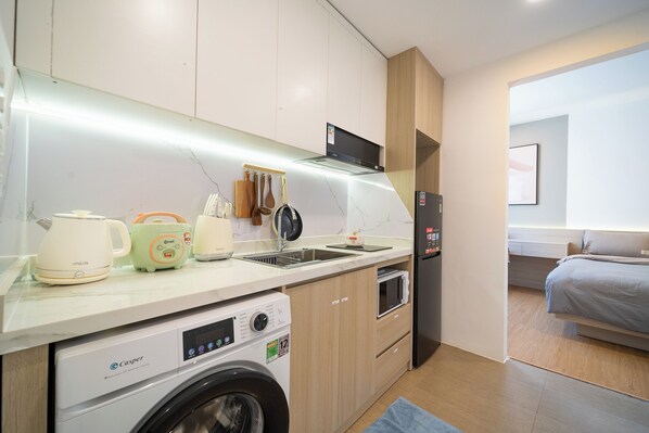 A compact kitchen with a washing machine, a refrigerator, and a microwave.
