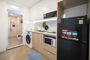 A compact kitchen with a washing machine, microwave, and a black refrigerator. - TAGO Ruby Hotel & Apartment Saigon (Ho Chi Minh City)