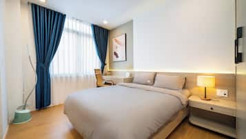 Habitación de hotel con una cama grande, una mesita de noche con lámpara, una silla, un escritorio y una ventana con cortinas.