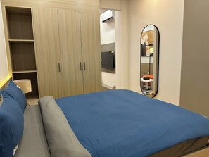 A bedroom with a bed, a wardrobe, a mirror, and a television.