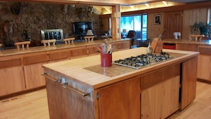 A spacious kitchen with a large island, wooden cabinets, a stone accent wall, and a stone fireplace. - Dolores River "BIG House" 8BR Cabin 300-Acre Private Ranch (Dolores)
