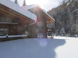 Eine Holzhütte mit schneebedecktem Dach, umgeben von verschneiten Bäumen.