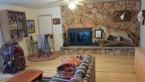A living room with a stone fireplace, a sofa, a coffee table, and a ceiling fan. - Dolores River "BIG House" 8BR Cabin 300-Acre Private Ranch (Dolores)