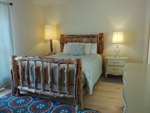 Ein Schlafzimmer mit einem rustikalen Bettgestell aus Holz, zwei Nachttischlampen, einem gemusterten Teppich und einem kleinen Nachttischchen mit Lampe.