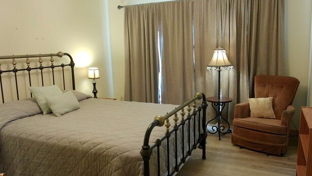 A bedroom with a bed, a chair, a lamp, and a window with curtains. - Dolores River "BIG House" 8BR Cabin 300-Acre Private Ranch (Dolores)