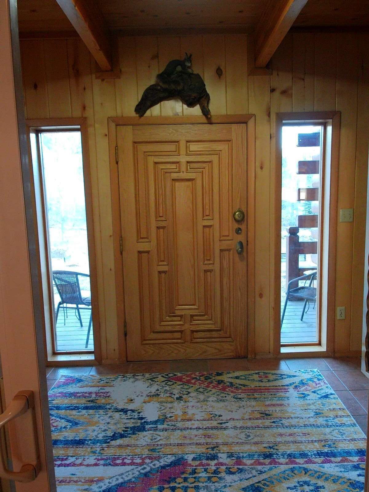 A wooden door with a decorative top, a patterned rug, and a view of outdoor furniture through a glass door.