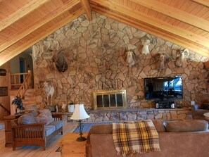 A cozy living room with a stone wall, a fireplace, a television, and a staircase leading to another level. - Dolores River "BIG House" 8BR Cabin 300-Acre Private Ranch (Dolores)