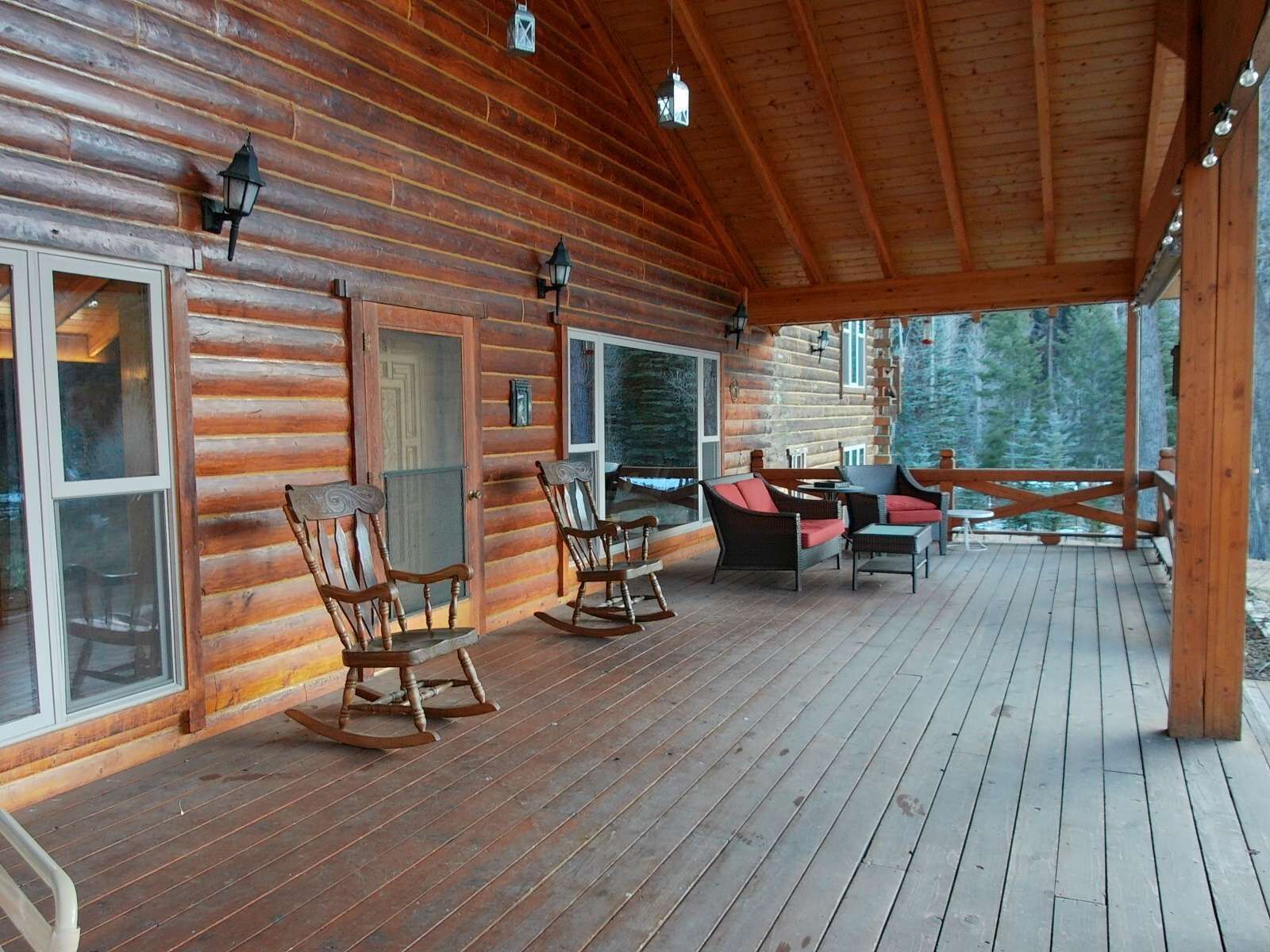 Eine Blockhütte mit einer Holzterrasse, Schaukelstühlen und einem Essbereich.