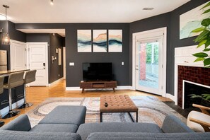 A modern living room with a flat-screen TV, grey sofas, a coffee table, and artwork on the wall. - King 1BR Opposite SLU Hospital Balcony  Parking (St. Louis)