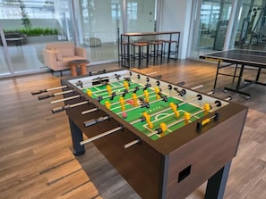 Una mesa de fútbolín en un espacio interior moderno, con piso de madera y paredes de vidrio.