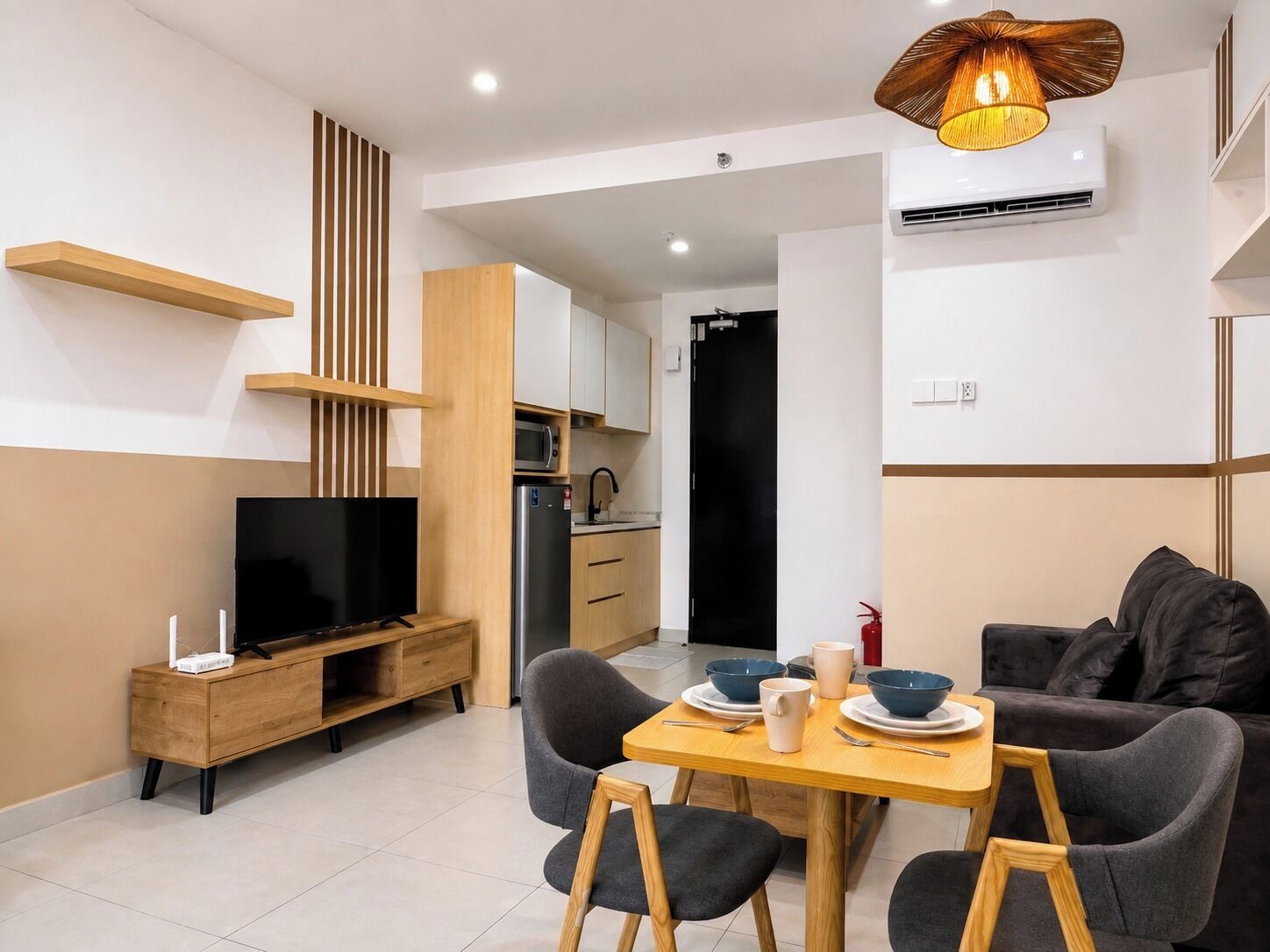 Un espacio habitable moderno con televisor, muebles de madera, un área de comedor con platos y tazones, y una cocina al fondo.
