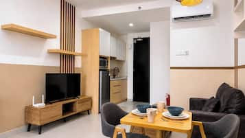 Un espacio habitable moderno con televisor, muebles de madera, un área de comedor con platos y tazones, y una cocina al fondo.