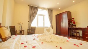 Una habitación de hotel con cama, escritorio, armario y ventana con cortinas.