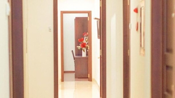 Un pasillo con un marco de puerta de madera, una silla y un florero con flores rojas.