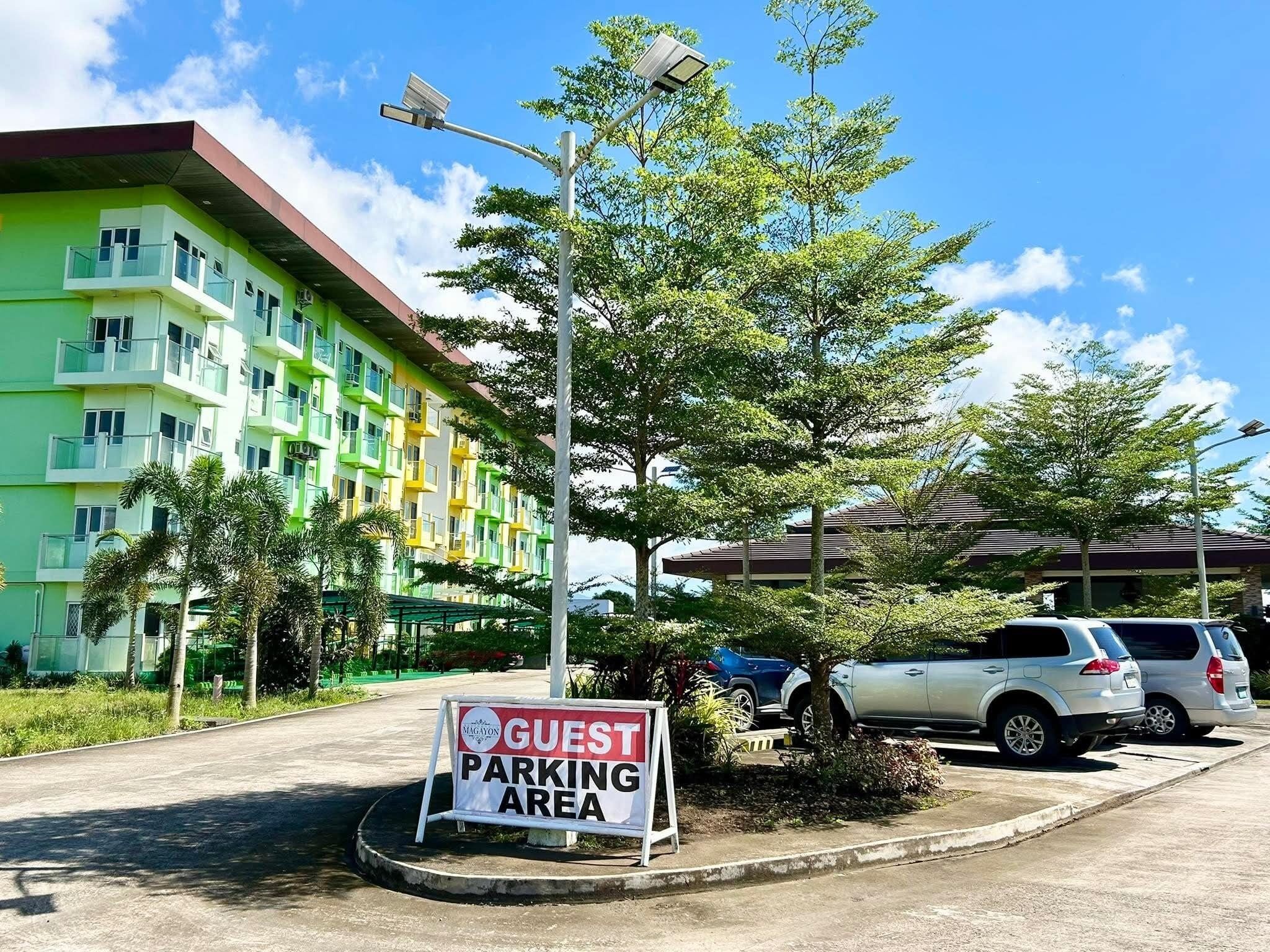 A guest parking area with a sign, a multi-story building, and parked cars.