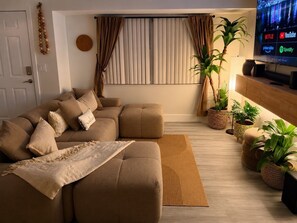 A living room with a sectional sofa, a flat-screen TV, and potted plants. - Palm Vibe House - Pool • Near Beach • Florida (Port St. Lucie)
