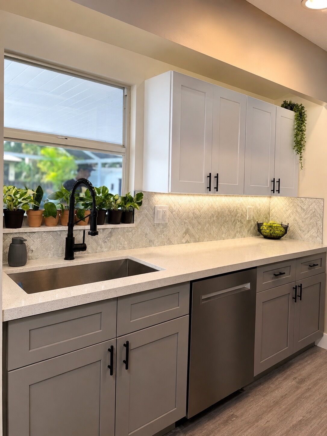 A kitchen with a large window, a sink, cabinets, and a countertop.
