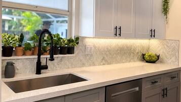 A kitchen with a large window, a sink, cabinets, and a countertop.
