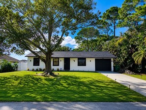Eingeschossiges Haus mit einem großen Baum im Vorgarten, einer Garage und einem gepflegten Rasen.