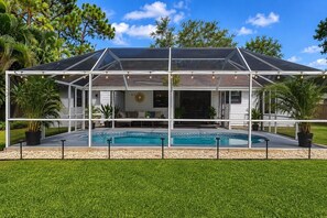 Ein Haus mit überdachter Terrasse, einem Swimmingpool und einem Rasen.
