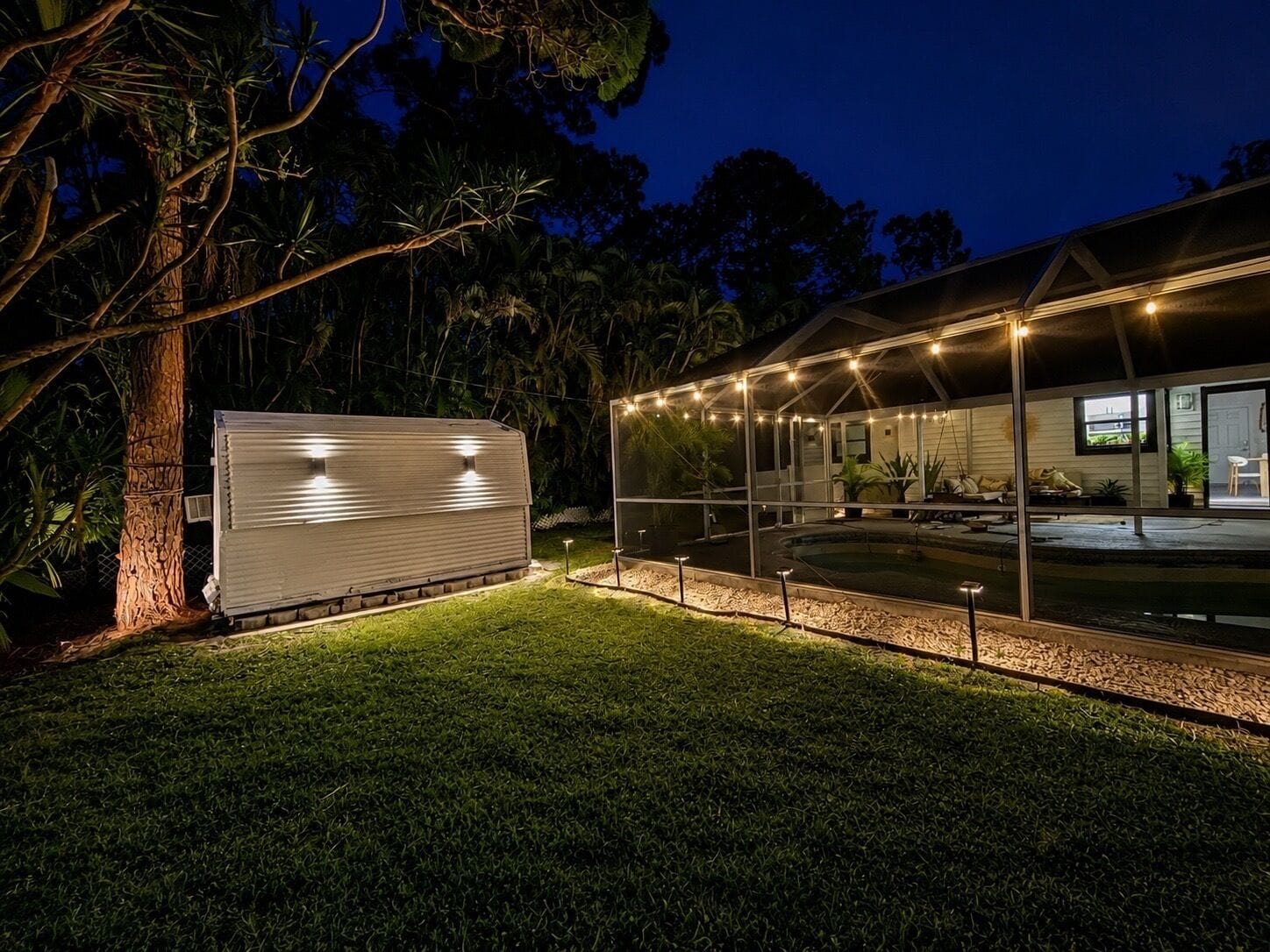 A house with a swimming pool, a covered patio, and a large tree.