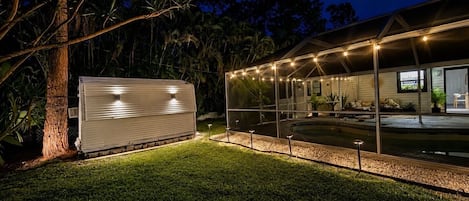 A house with a swimming pool, a covered patio, and a large tree.