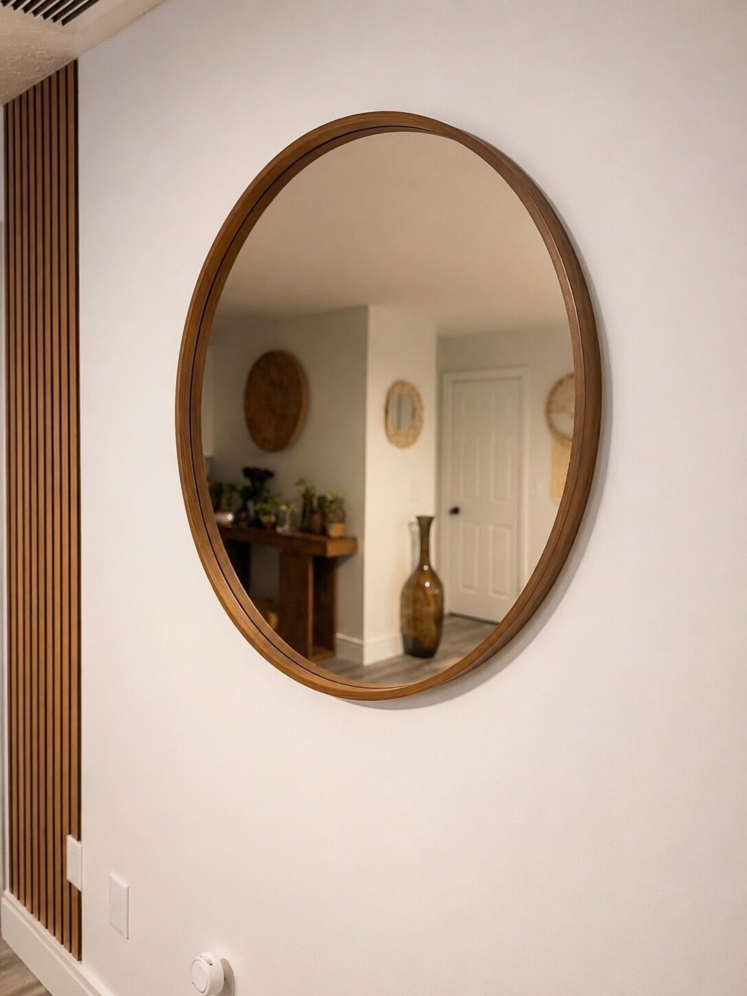 A round mirror with a wooden frame on a white wall.