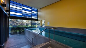 En modern inomhuspool med fri utsikt över omgivningen, en gul vägg och en säkerhetsskylt.