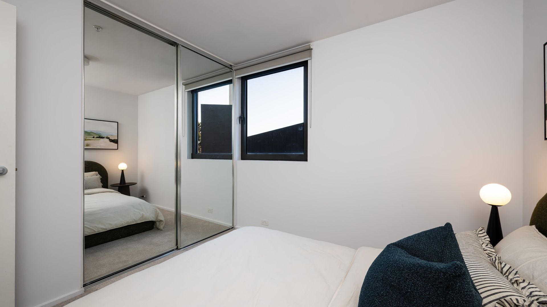 A bedroom with a bed, bedside lamps, a window, and a mirror.