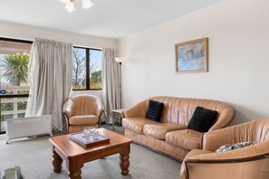Une pièce avec un canapé en cuir, une table basse en bois et un fauteuil. Il y a un tableau au mur et une fenêtre avec des rideaux.