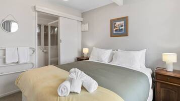 A hotel room with a bed, a bedside table with a lamp, a bathroom with a shower, and a mirror on the wall.