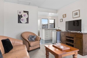 Ein Wohnzimmer mit einer Ledersofa, einem Holztisch und einem Fernseher auf einem Holzschrank.