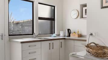 A compact kitchen with a window, a sink, a kettle, a toaster, and a basket.