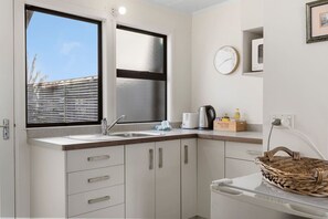 Eine kleine Küche mit Fenster, einer Spüle, einem Wasserkocher, einem Toaster und einem Korb.