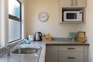 Eine Küche mit Spüle, Wasserkocher, Toaster, Mikrowelle, einer Uhr und einer Holzkiste mit der Aufschrift 'VETRO'.