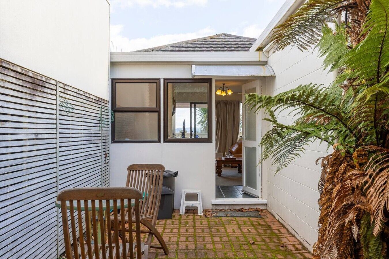 A small outdoor patio with a table and chairs, a white wall, and a door leading to an interior space.
