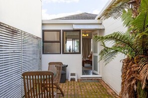 Une petite terrasse extérieure avec une table et des chaises, un mur blanc et une porte donnant sur un espace intérieur.