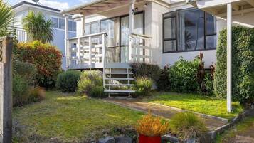 Uma casa moderna com varanda coberta, um pequeno jardim com diversas plantas e um vaso vermelho em primeiro plano.