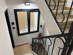 A staircase with a black metal railing, a window with a black frame, and a fire extinguisher on the wall. - Ground floor with A/C and terrace only 250m beach (Calella)