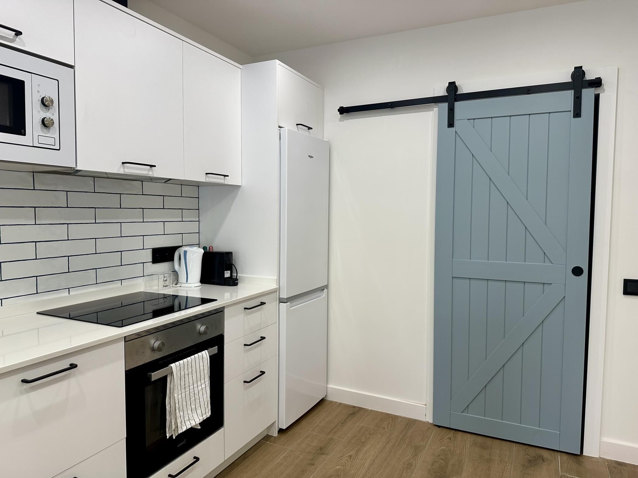 A modern kitchen with white cabinetry, a black stove, and a blue sliding door.