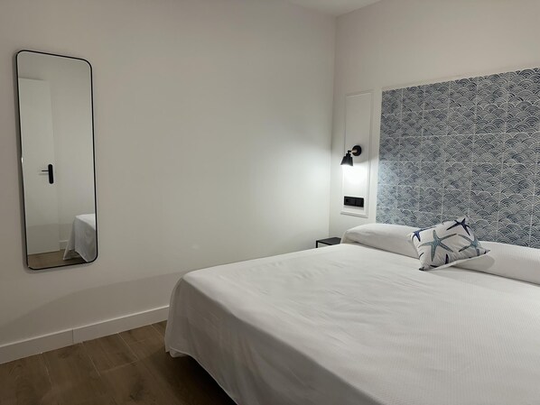 A hotel room with a large bed, a bedside table, a nightstand, a wall-mounted mirror, and a patterned headboard. - Ground floor with A/C and terrace only 250m beach (Calella)