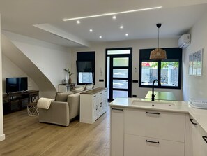 A modern living room with a sofa, TV, and a dining area with a table and chairs. - Ground floor with A/C and terrace only 250m beach (Calella)