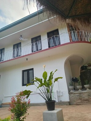 Un edificio de dos pisos con un balcón, plantas en macetas y techo de paja.