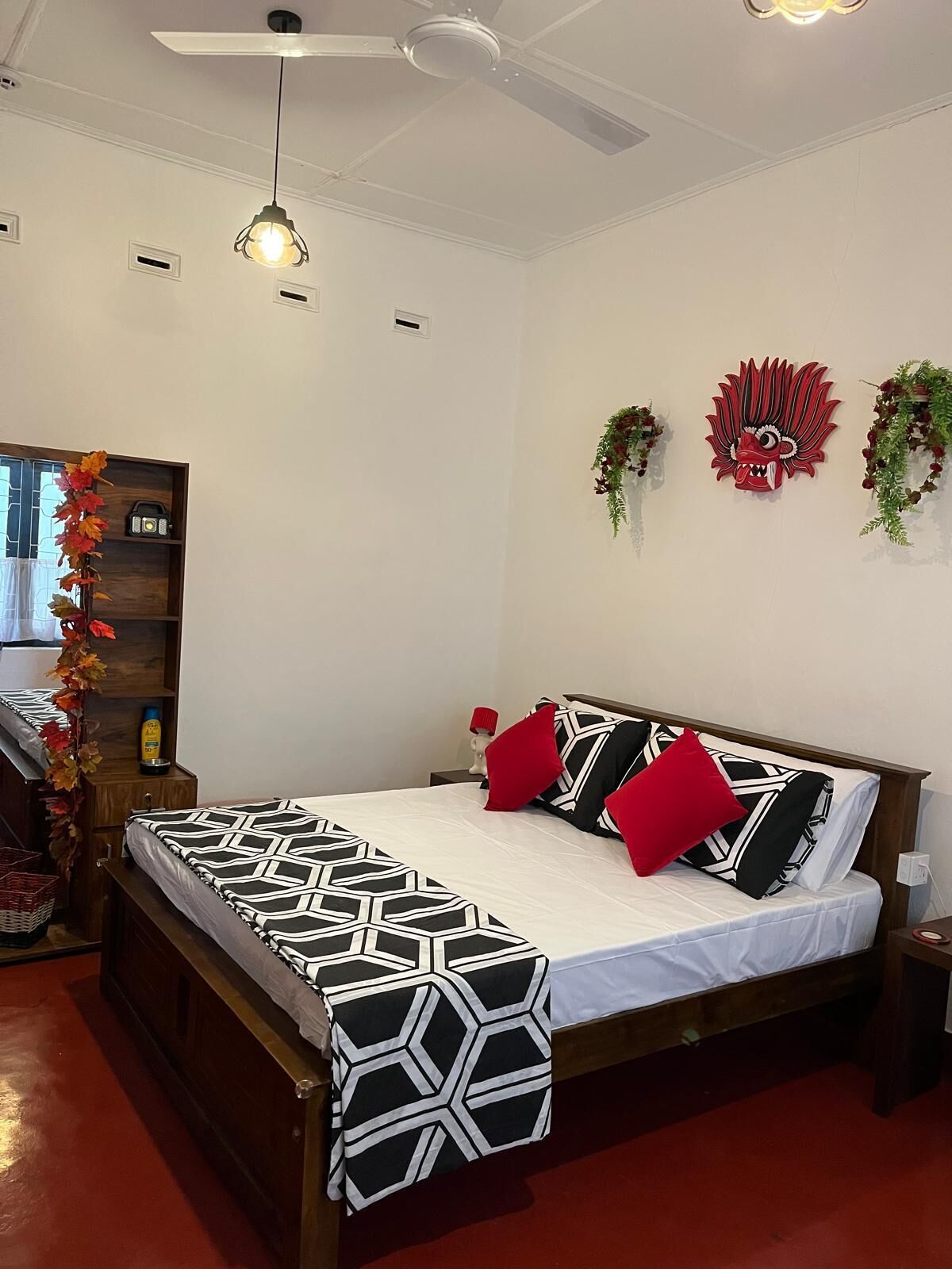 Une chambre à coucher comprenant un lit, un ventilateur de plafond, un luminaire fixé au mur et un élément décoratif au niveau de la tête de lit.