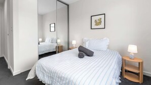 Een hotelkamer met een groot bed, twee nachtkastjes met lampen, een spiegel en een lijst met een afbeelding aan de muur.