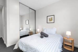Ein Hotelzimmer mit einem großen Bett, zwei Nachttischen mit Lampen, einem Spiegel und einem gerahmten Bild an der Wand.