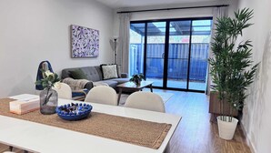 Een moderne woonkamer met een bank, een salontafel en een eethoek met tafel en stoelen. Er is een schuifdeur die leidt naar een terras met uitzicht.