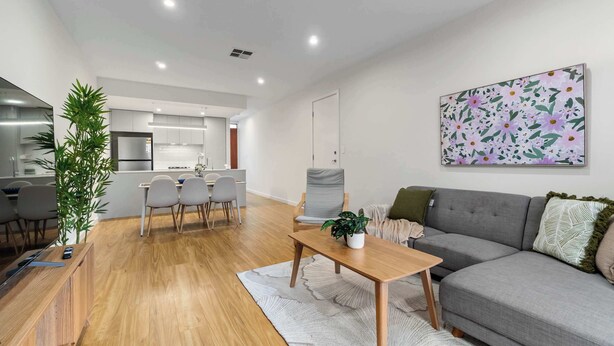 Een moderne woonkamer met een grijze bank, een houten salontafel en een eethoek met stoelen en een tafel.