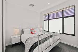 A bedroom with a bed, two bedside tables, a window with blinds, and a ceiling vent. - Campbelltown modern home Family Stay (Campbelltown)